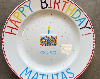May include: White ceramic plate with a colorful "Happy Birthday!" message and the name "Mathias" in blue. The plate features a cake illustration with a lit candle and confetti. The date "02-13-2025" is also printed on the plate.