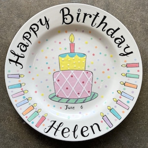 May include: White ceramic plate with a colorful birthday cake and candles. The plate has the words "Happy Birthday" and "Helen" written on it. The date "June 6" is also written on the plate.