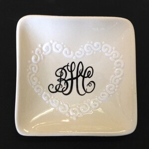 May include: White ceramic ring dish with a raised heart design and a black monogram "BHC" in the centre.