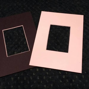May include: Two picture frames, one brown and one pink, with white mats and rectangular openings.