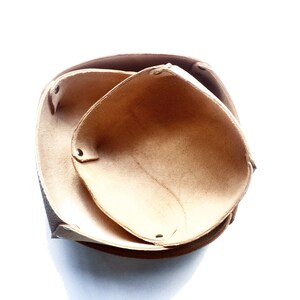 May include: Two brown leather bowls nested together. The bowls are made of a soft, suede-like material and have a natural, rustic look.