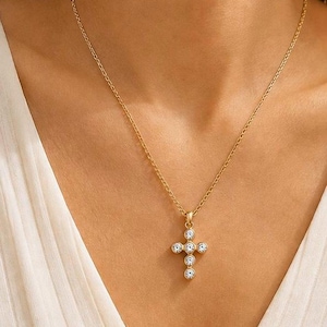 Op de afbeelding: Een goudkleurige ketting met een fijne schakelketting en een kruisvormige hanger. De hanger is versierd met zes heldere, rondgeslepen stenen in een verticale en horizontale opstelling, wat zorgt voor een klassiek en verfijnd sieraad.