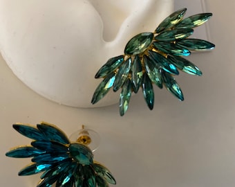 May include: A pair of fan-shaped ear climbers featuring marquise-cut crystals in shades of teal, emerald, and forest green. The crystals are arranged in a radiating pattern on a gold-tone metal base, with one earring displayed on a white ear form.