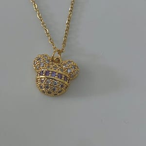 May include: A gold chain necklace with a small, sparkly Mickey Mouse pendant. The pendant is covered in clear and purple rhinestones.