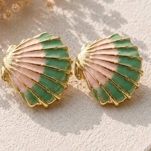 Könnte beinhalten: Ein Paar muschelförmige Ohrringe mit abwechselnden Segmenten aus pastellrosa und salbeigrünem Emaille. Das Design ist mit goldfarbenen Metallrippen akzentuiert, die den natürlichen strahlenförmigen Linien der Muschelstruktur folgen.