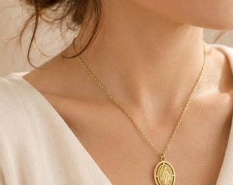 May include: A gold-toned necklace featuring a delicate chain and an oval-shaped pendant. The pendant displays a central embossed figure within a raised border, suspended from a simple jump ring attached to the fine link chain.