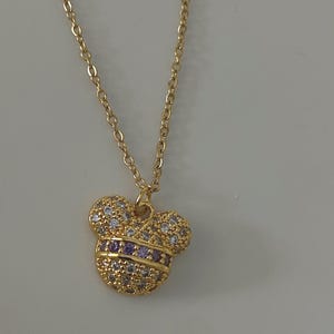 May include: A gold chain necklace with a small, sparkly Mickey Mouse pendant. The pendant is covered in clear and purple rhinestones.