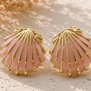 Peut inclure: Une paire de boucles d'oreilles en forme de coquilles Saint-Jacques, dotées d'une monture en métal doré poli avec des nervures en relief et un émail rose clair lisse remplissant les sections entre les lignes métalliques, créant un motif texturé.