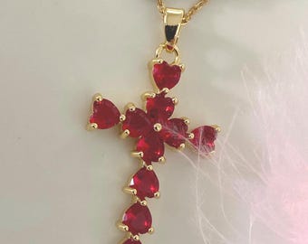 Op de afbeelding: Gouden ketting met een rode hartvormige kruis hanger. Het kruis is gemaakt van meerdere kleine rode hartvormige stenen.