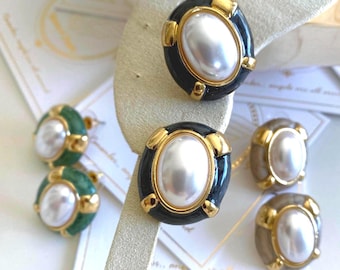 May include: A collection of oval-shaped stud earrings featuring a central white faux pearl cabochon surrounded by a gold-tone metal frame. The earrings are available in black, green, and beige enamel finishes, each secured with a post backing.