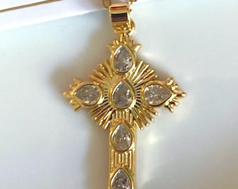 May include: Gold-toned cross pendant necklace with clear teardrop-shaped stones. The cross features a sunburst design and is suspended from a delicate chain. The background includes the words "Remember... angels are..."