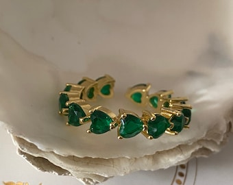 May include: Gold ring with a band of green heart-shaped stones. The ring is on a white background with the text "Victory of Angels" in gold lettering.