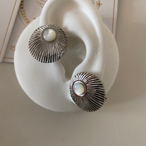 May include: A pair of silver earrings with a white mother-of-pearl center. The earrings have a sunburst design.