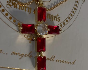 Op de afbeelding: Een goudkleurige kruishanger aan een ketting met vier rechthoekige rode stenen en een centrale ronde heldere steen. De hanger wordt gepresenteerd op een witte kaart met de tekst Victory Angels en angels all around in gouden letters.