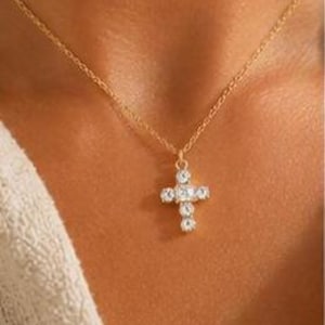 Op de afbeelding: Een goudkleurige ketting met een kruishanger. Het kruis is versierd met vijf heldere, rondgeslepen stenen die in een verticaal en horizontaal patroon zijn geplaatst, wat zorgt voor een sprankelend middelpunt aan een fijne schakelketting.