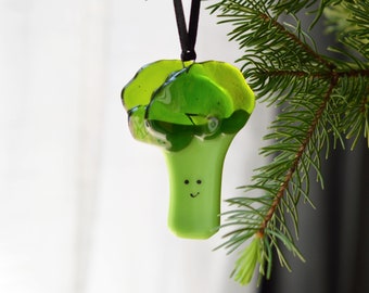 May include: A green glass ornament shaped like a smiling broccoli with a black string for hanging.