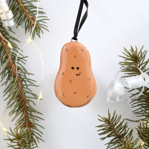 May include: A brown glass ornament shaped like a potato with a smiling face. The ornament has a black string for hanging.