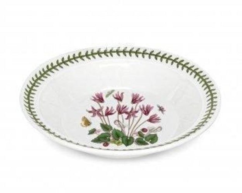 May include: A white ceramic bowl with a green border and a floral design featuring pink cyclamen flowers. The bowl is perfect for serving soup, salad, or pasta.