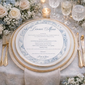 May include: A wedding dinner menu on a white plate with a gold rim, featuring a blue floral design. The menu includes starter, main course, and dessert options. The date 05.30.2023 is printed at the bottom.