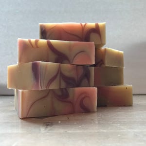 May include: A stack of six handmade soap bars with a swirl pattern in shades of pink, white, and purple.