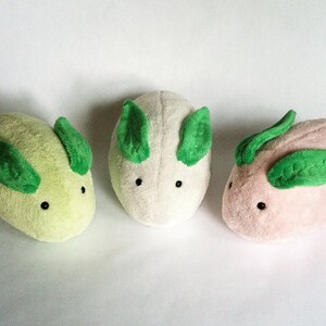 May include: Three plush toys shaped like a cartoon animal with green leaf ears. The toys are green, white, and pink.