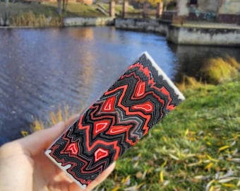 May include: A rectangular block featuring a vibrant, multi-layered pattern of wavy, interlocking lines in bold red, charcoal gray, and black, creating a striking visual effect across the entire surface of the object.