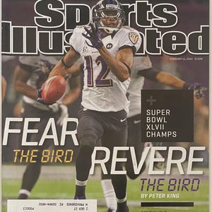 Può includere: Copertina della rivista Sports Illustrated con un giocatore di football americano con una divisa viola e nera, che corre con il pallone. Il testo della copertina recita "Fear the Bird Revere" e "Super Bowl XLVII Champs".