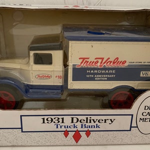 May include: A white and blue 1931 delivery truck bank with the words "True Value Hardware 10th Anniversary Edition" on the side. The truck has red wheels and a black roof. The box is white with red and blue accents.