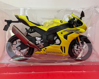 May include: A yellow Honda motorcycle model with black accents and a clear plastic display case. The motorcycle has a black exhaust pipe and the word "HONDA" is printed on the side.