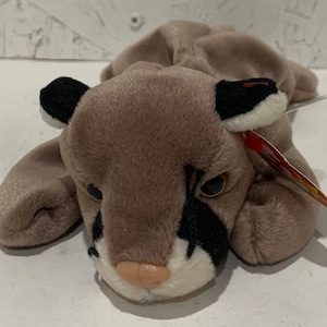 May include: A brown and black plush toy cougar with a white belly and a red Ty tag. The toy is lying on its belly with its head turned to the side.