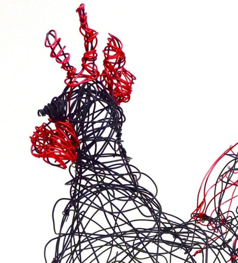 May include: A wire sculpture of a rooster, crafted from black and red wire. The rooster's comb and wattle are red, while the body is black. The sculpture is set against a white background, highlighting the intricate wirework.
