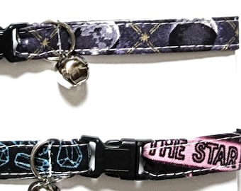 May include: Five cat collars with black plastic buckles and silver bells. The collars feature various patterns, including celestial designs, geometric shapes, and text that reads "SEVEN" and "THE STAR".