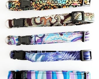 Op de afbeelding: Vijf halsbanden voor huisdieren met patronen, zwarte plastic gespen en metalen D-ringen. De halsbanden hebben verschillende ontwerpen, waaronder een luipaardprint, paisley en bloempatronen in bruin, blauw, paars en blauwgroen. De halsbanden worden tegen een witte achtergrond weergegeven.