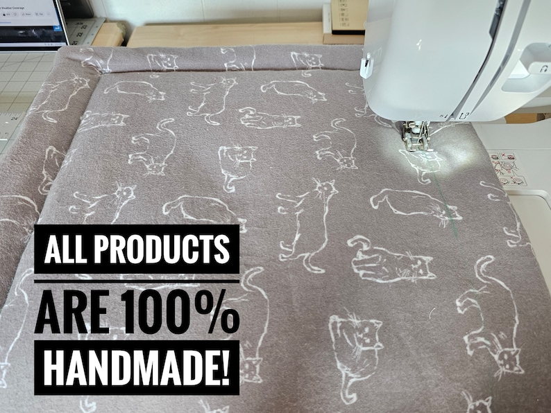May include: A gray cat-themed fabric being sewn with a white sewing machine. The fabric has a repeating pattern of white cat illustrations. Text on the image reads: ALL PRODUCTS ARE 100% HANDMADE!