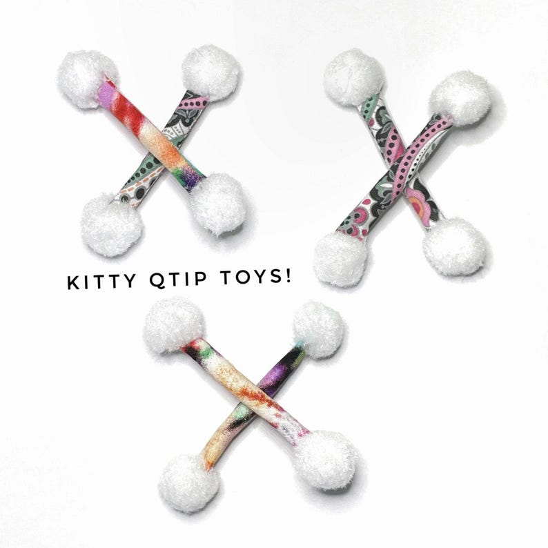 Pode incluir: Uma cole&ccedil;&atilde;o de brinquedos para gatos. Cada brinquedo apresenta um bast&atilde;o estampado com um pompom branco fofo em cada extremidade. O texto "KITTY QTIP TOYS!" &eacute; exibido em letras pretas.