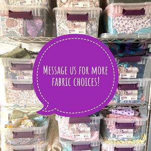 May include: Clear plastic storage bins filled with various fabrics, stacked on metal shelving. The bins have purple handles and labels. A purple speech bubble with white text reads "MESSAGE US FOR MORE FABRIC CHOICES!"