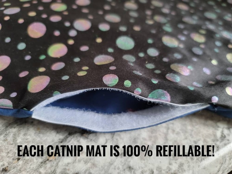 May include: Close-up of a black catnip mat with iridescent, colorful polka dots. The mat has a white opening and the text "EACH CATNIP MAT IS 100% REFILLABLE!"