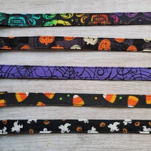 May include: A collection of Halloween-themed ribbons with various patterns. Designs include pumpkins, candy corn, ghosts, and spiderwebs. The ribbons are black, purple, and white, with orange, green, and yellow accents. These ribbons are ideal for crafting and seasonal decorations.