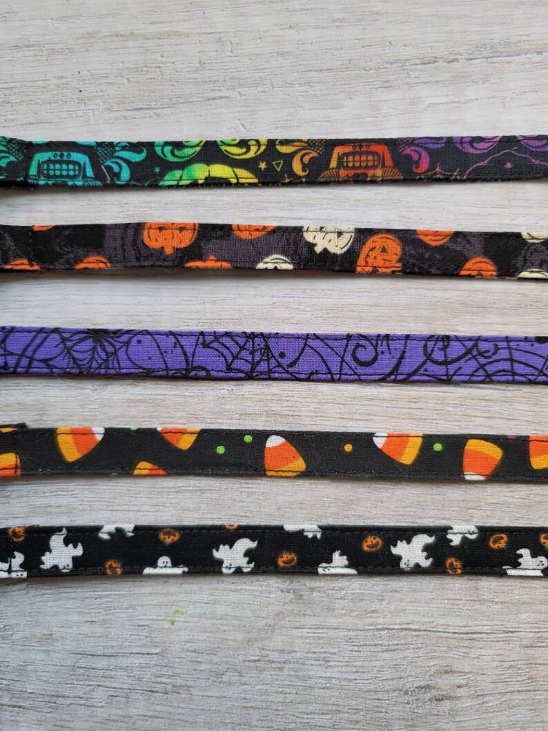 May include: A collection of Halloween-themed ribbons with various patterns. Designs include pumpkins, candy corn, ghosts, and spiderwebs. The ribbons are black, purple, and white, with orange, green, and yellow accents. These ribbons are ideal for crafting and seasonal decorations.