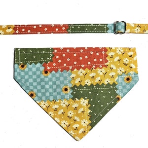 May include: A patchwork cat collar and bandana set. The collar has a black buckle and a small bell. The bandana and collar feature a mix of floral and geometric patterns in yellow, green, red, and blue.