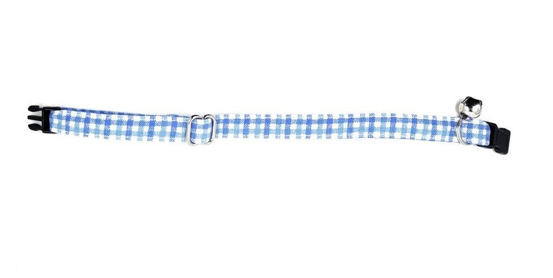 May include: A blue and white gingham cat collar with a silver-colored bell and a black plastic buckle. The collar is approximately 0.5 inches wide.