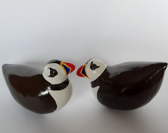 May include: Two ceramic puffins facing each other. The puffins are painted brown, white, black, yellow, red, and blue.