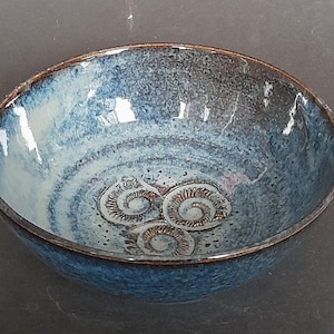 May include: A blue and white glazed ceramic bowl with a dark brown rim. The bowl has three spiral designs at the base. Suitable for serving food or as a decorative item. Measurements in cm.