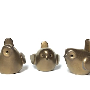 May include: Three small, gold-coloured ceramic bird figurines. The birds are facing different directions and have a glossy finish.