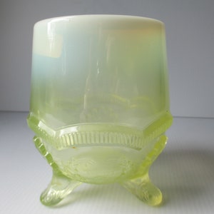 May include: A clear glass vase with a green and white ombre effect. The vase has a scalloped rim and three feet.