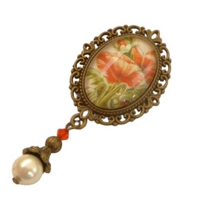 以下が含まれることがあります： 繊細なゴールドトーンのフレームと赤いポピーの花のデザインが施されたヴィンテージスタイルのブローチ。ブローチにはパールと赤いビーズの垂れ下がりが付いています。