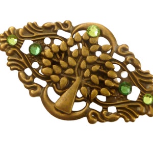 Könnte beinhalten: Eine goldfarbene Brosche aus Metall mit einem detaillierten Baumdesign und grünen Strasssteinen. Der Baum ist von einem dekorativen Filigranmuster umgeben.