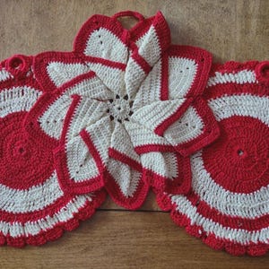 May include: Three crocheted items consisting of two circular red and white striped pot holders with scalloped edges and one central star-shaped piece featuring layered white petals with red trim, each including a small loop for hanging.