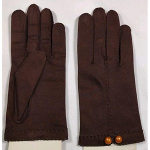May include: A pair of dark brown gloves featuring a smooth fabric construction with visible stitching along the fingers and cuffs. The wrist area of the right glove is accented with two small, round, orange-toned decorative beads.