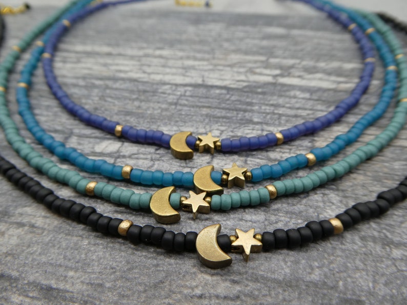 May include: Four layered necklaces with a crescent moon and star charm. The necklaces are made of small beads in shades of blue, teal, and black.